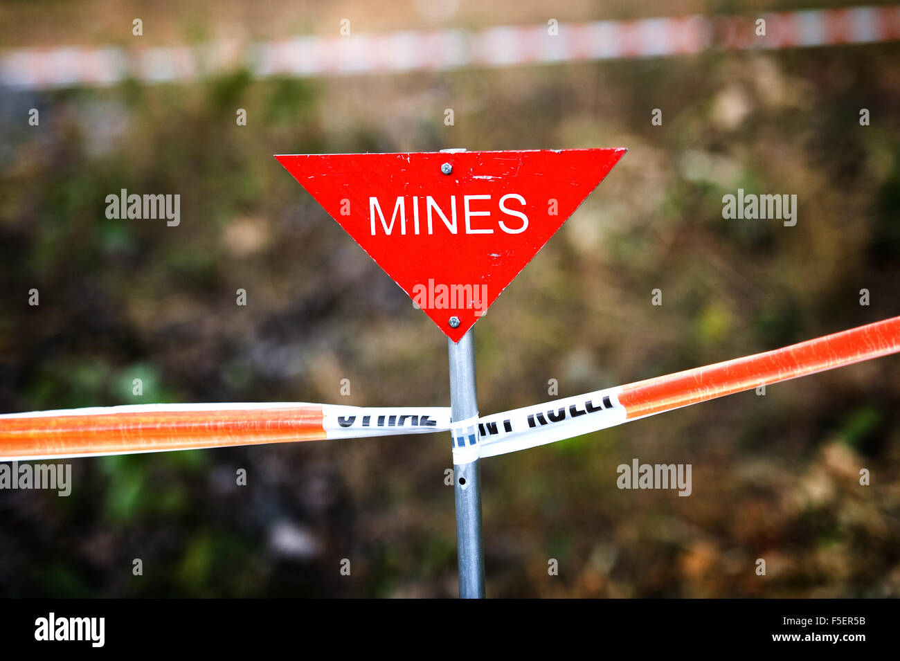 Triangular, red 'mines' sign on taped off mine field Stock Photo