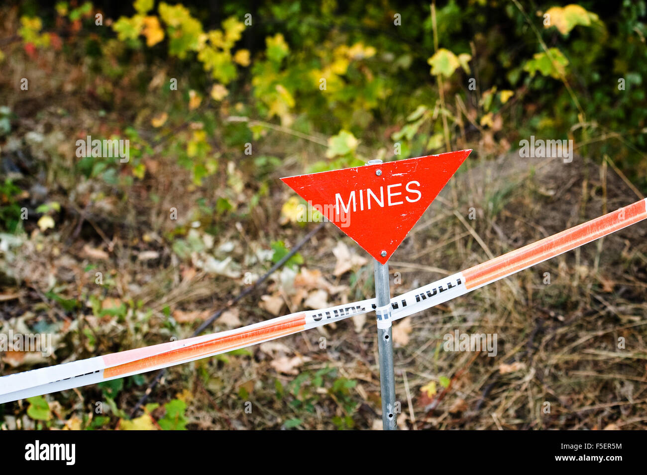 Triangular, red 'mines' sign on taped off mine field Stock Photo