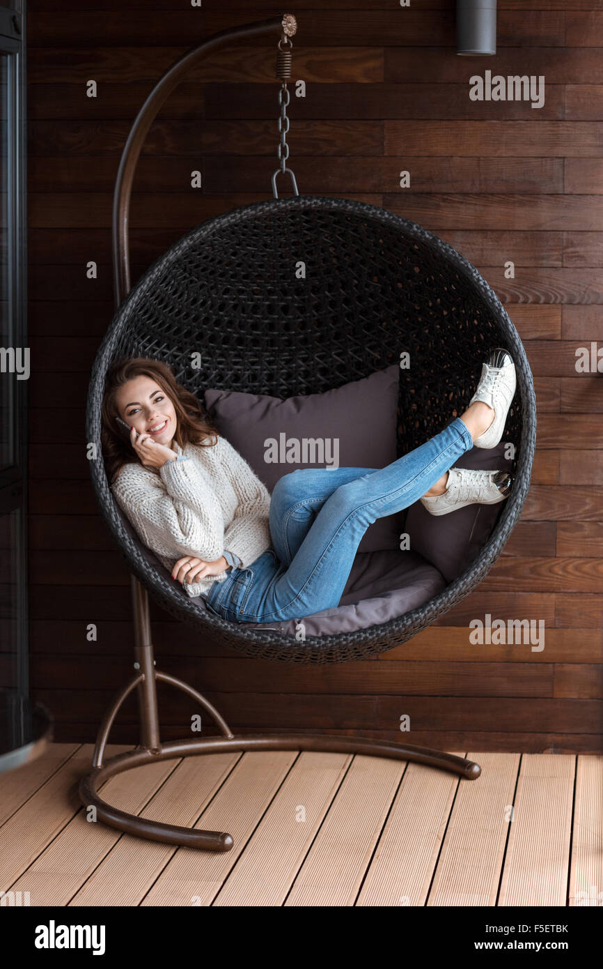 Young pretty smiling woman lying in rattan buble chair using smart phone Stock Photo