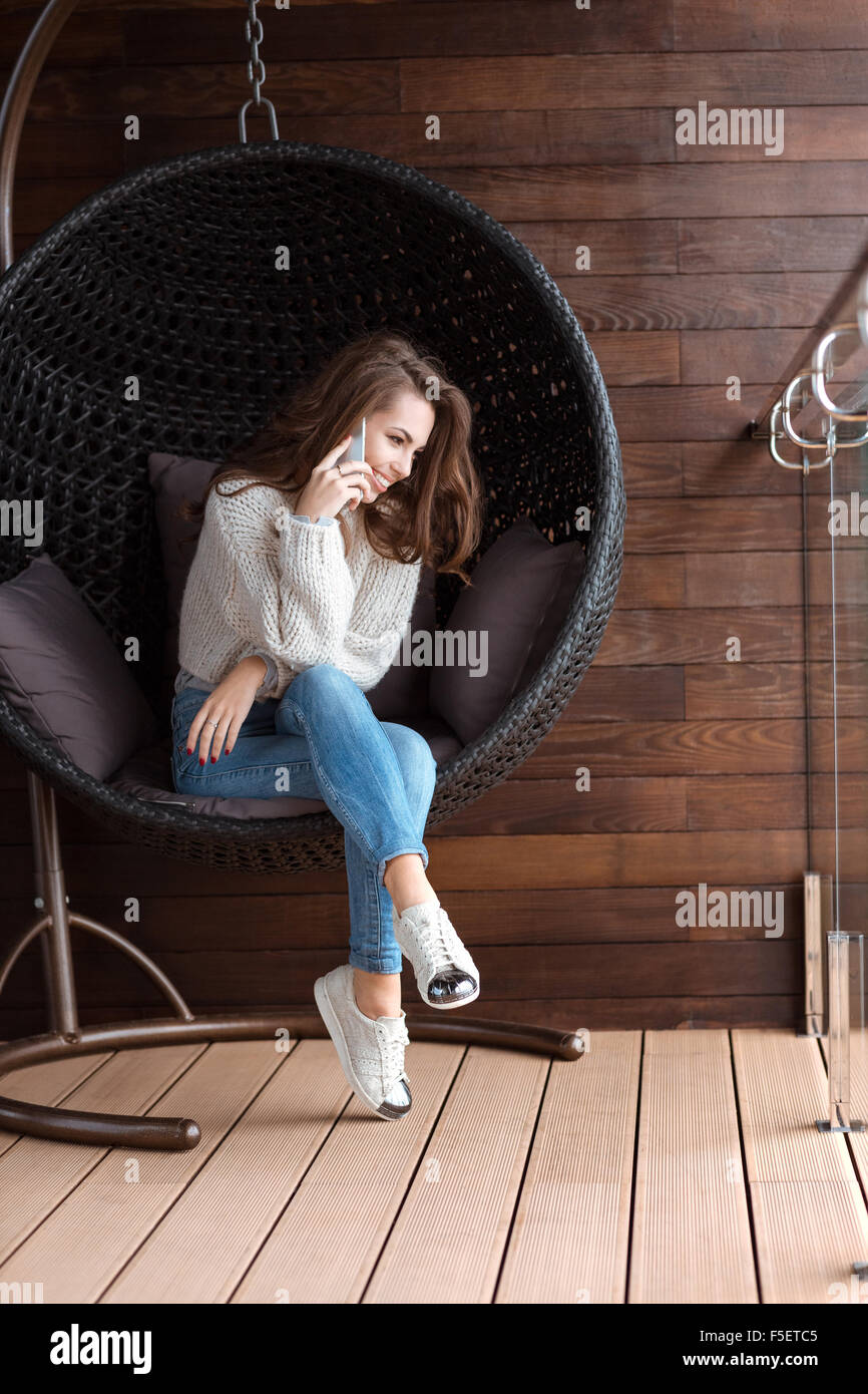 Cute positive girl sitting in bubble chair and talking on the cell phone Stock Photo