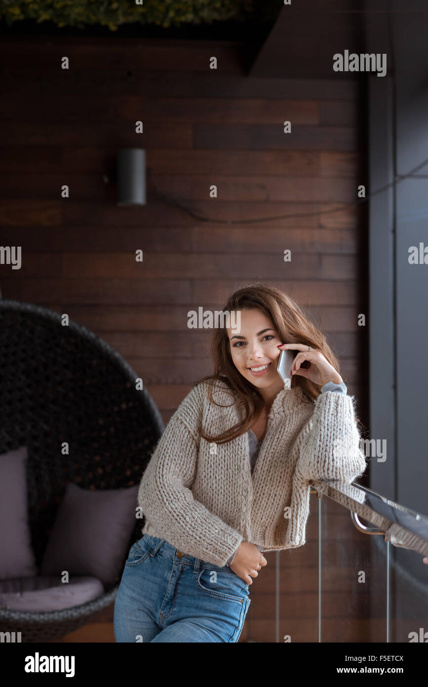 Happy pretty smiling young woman weared in sweater and jeans talking on mobile Stock Photo