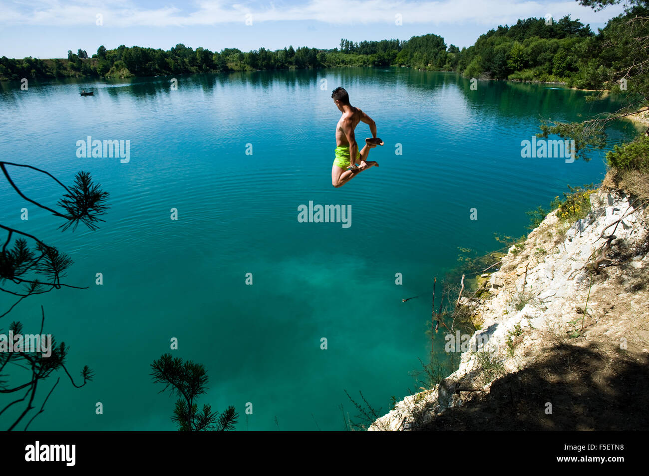 Young man jumps of the cliff to the clean, turquoise water. Sulejow, Poland. Stock Photo