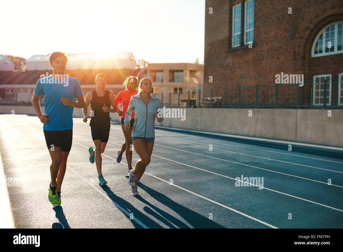 Professional runners running on a race track. Multiracial athletes practicing on race track in stadium on a bright sunny day. Stock Photo