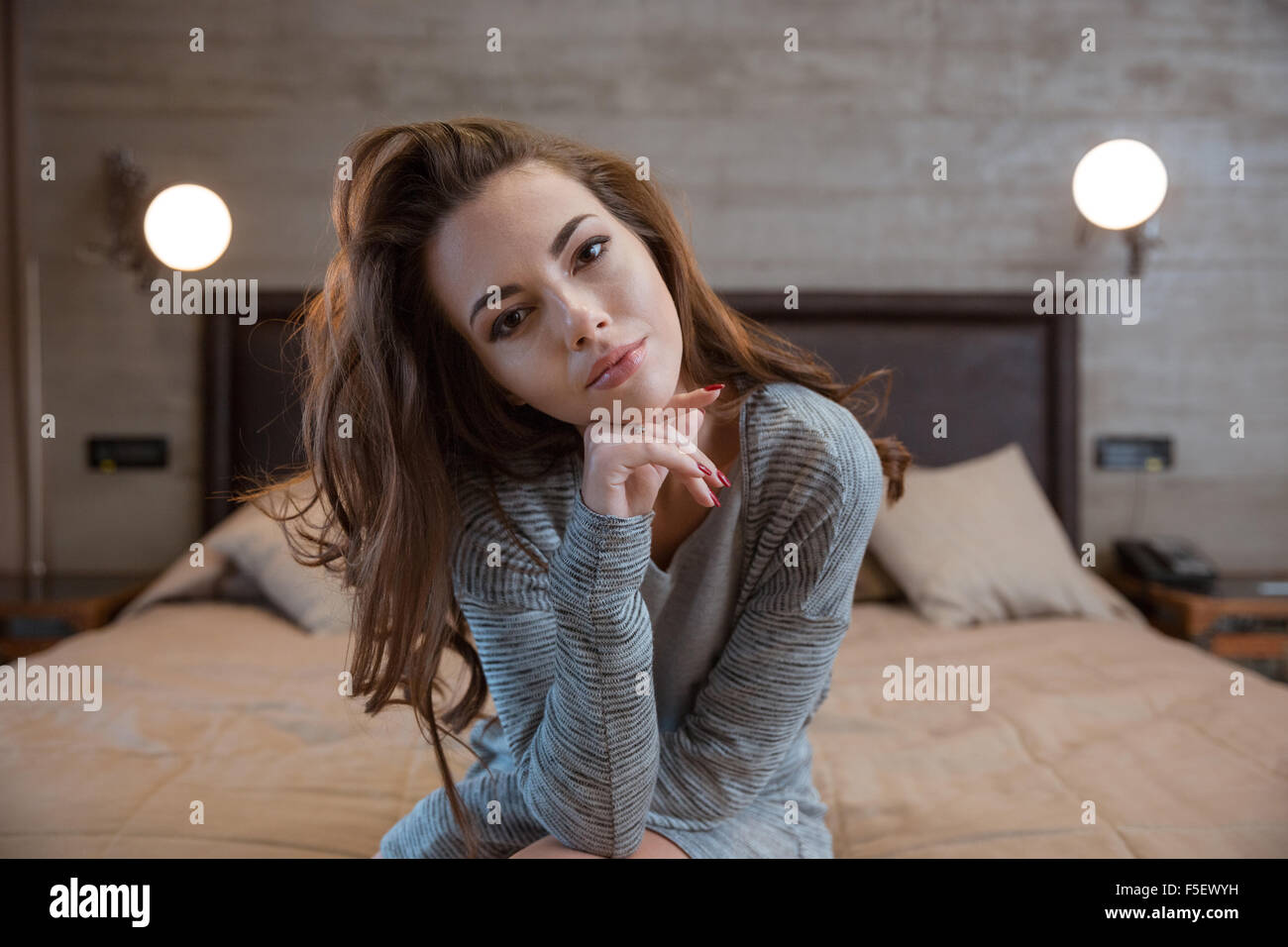 Portrait of a beautiful woman sitting on the bed at home and looking at ...