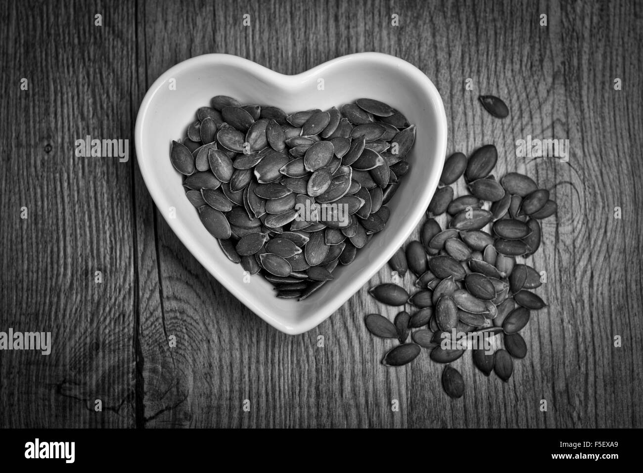 Pumpkin seeds in a heart shaped dish, black & white Stock Photo