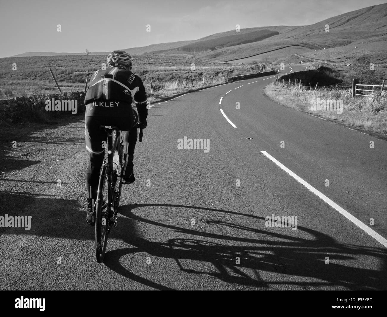 A single road cyclist in Ilkley colors on an empty road cycling towards hills Stock Photo