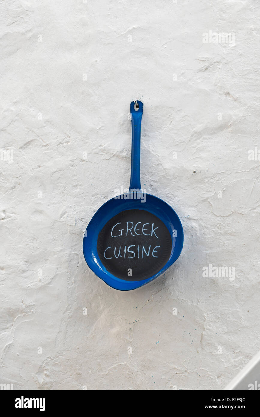 Pan hung on a whitewashed wall with the text 'Greek cuisine' Stock Photo