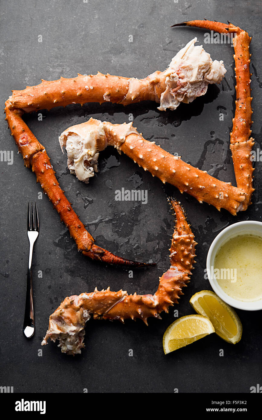 King crab legs arranged on a slate background with butter, lemons, and a seafood fork Stock Photo