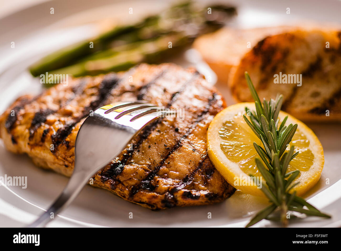 A grilled chicken breast  dinner on a plate with bread and asparagus, garnished with a lemon Stock Photo