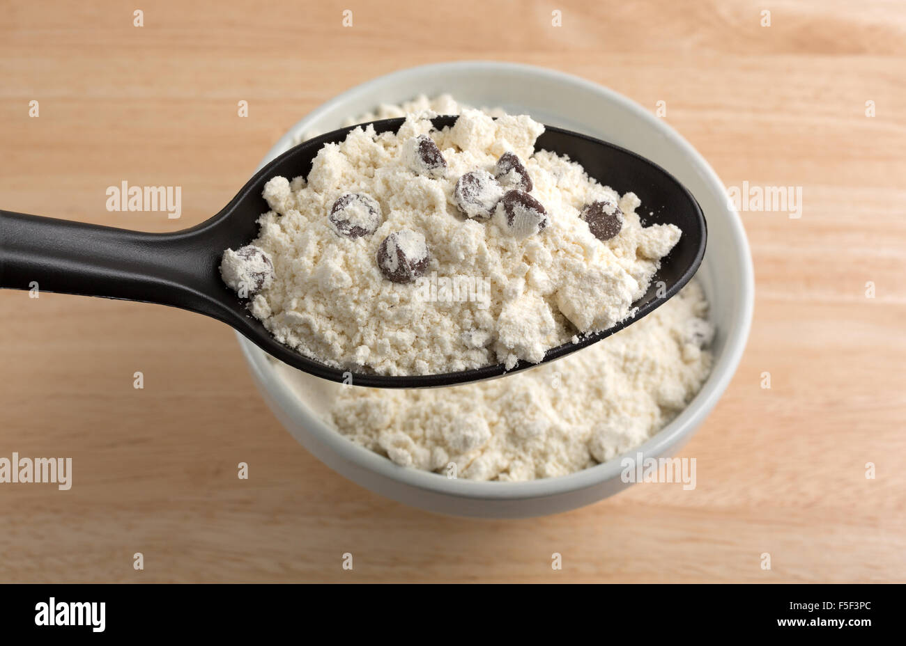 Dry chocolate chip cookie mix in an old bowl with a black handle filled spoon above atop a wood table Stock Photo