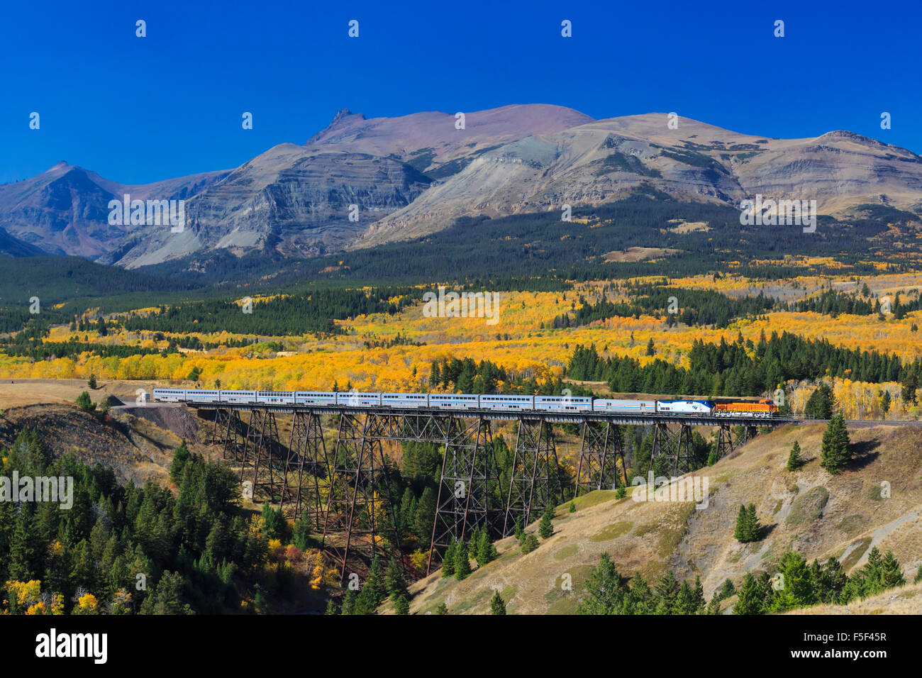 passenger train crossing over trestle in autumn below peaks of glacier