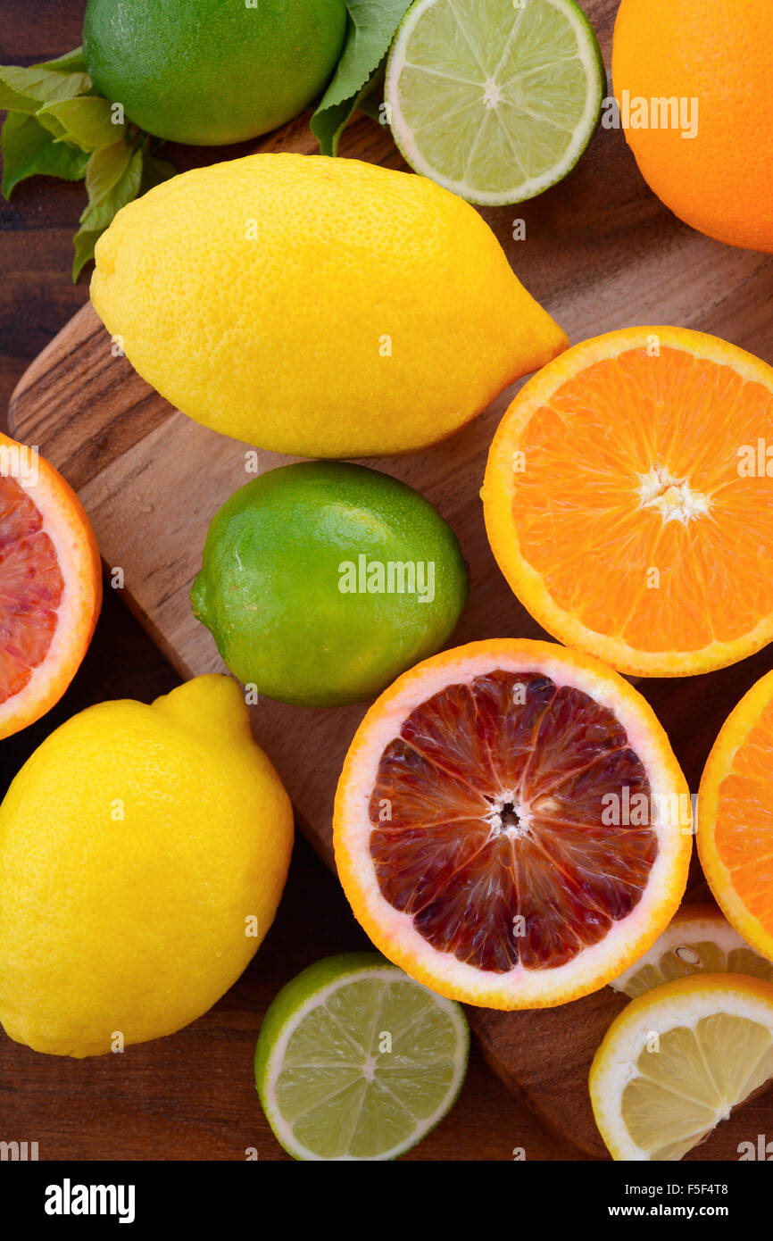 Mixed citrus fruit including navel and blood oranges, lemons and limes on dark wood table. Stock Photo