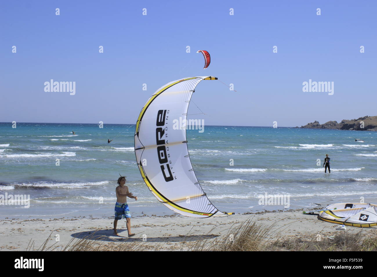 Swimmer trying to catch kite's struts while a surfer (in the sea) manouvres on Keros bay. Lemnos or limnos island, Greece. Stock Photo