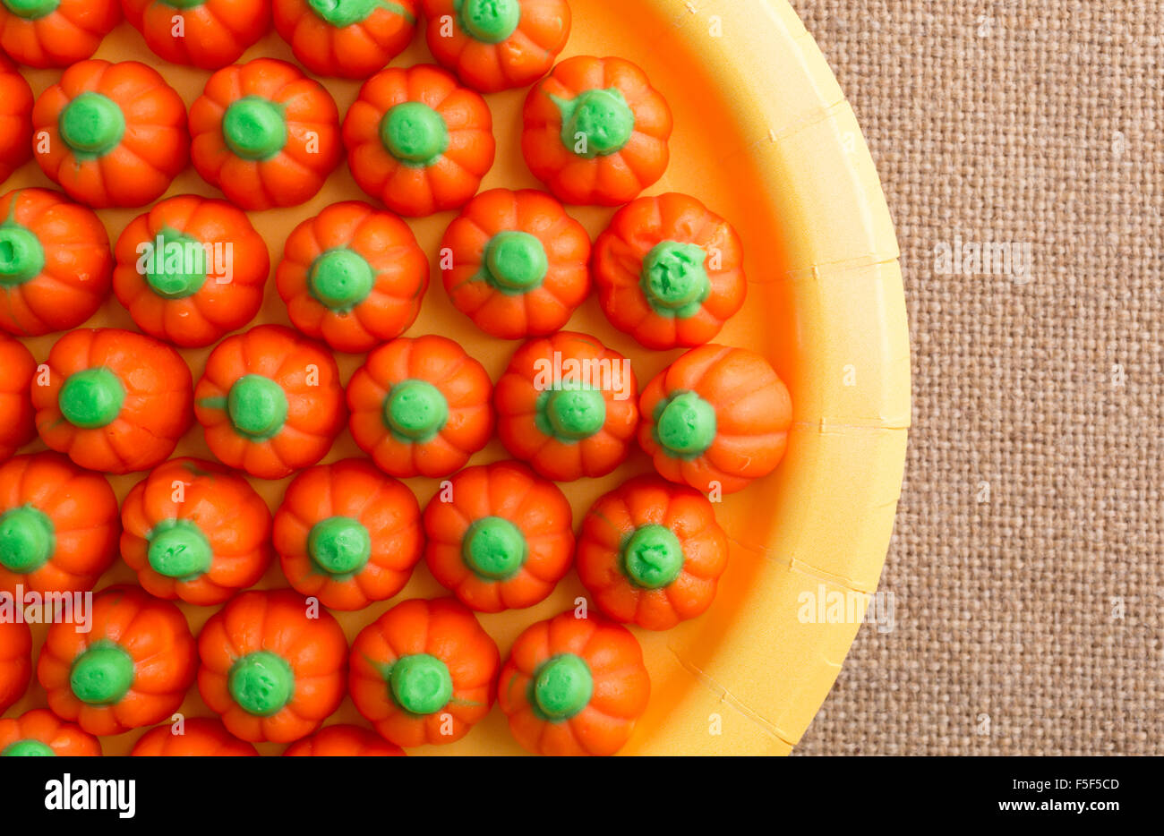 Top close view of orange and green Halloween pumpkin candy on a yellow paper plate atop a burlap tablecloth Stock Photo