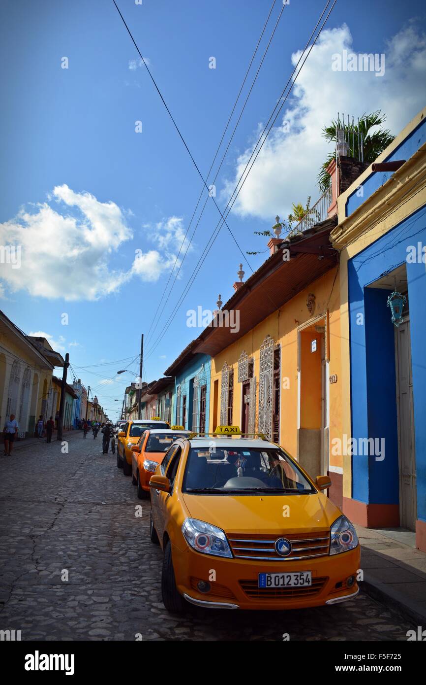 Yellow taxi cabs parked in a line in a cobbled street with colourful houses in Trinidad Cuba Stock Photo