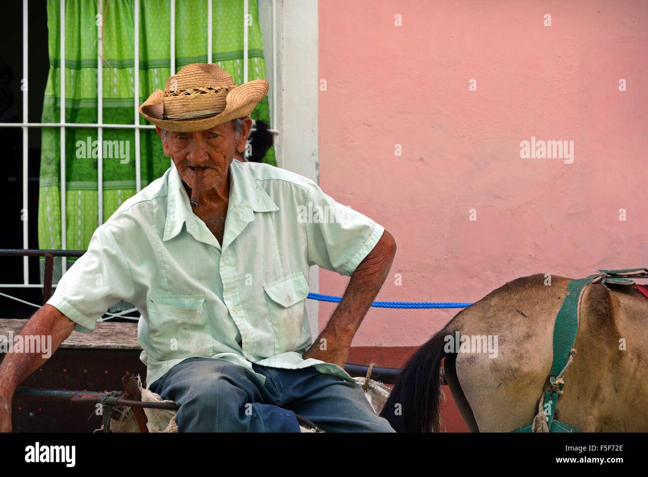 Old Cuban man sitting with cigar and his horse and cart in Trinidad Cuba staring at the camera Stock Photo