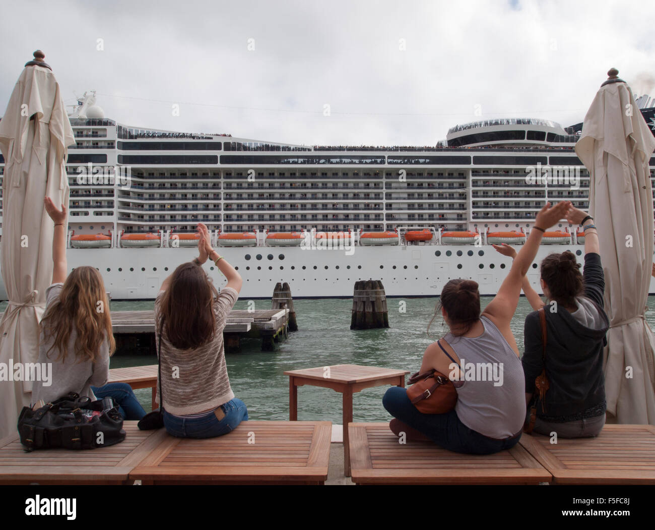 Tourists sitting at Canale della Giudecca in Venice, Italy, are waiving to the leaving cruise ship MSC Divina. Stock Photo