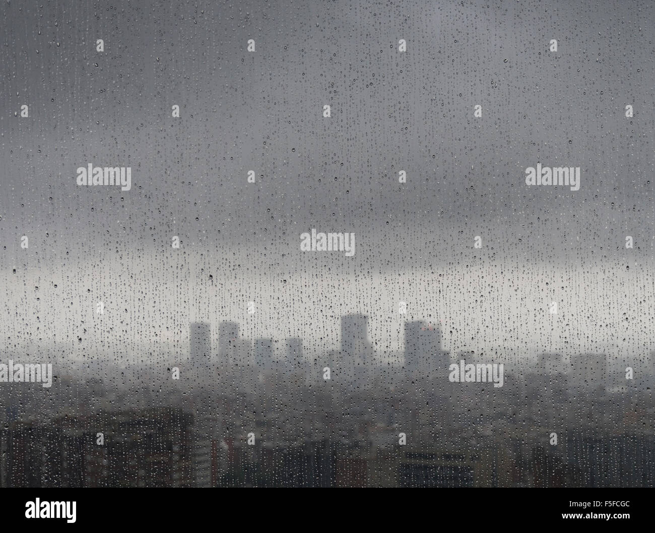 After heavy rainfall, the diffuse skyline of Barcelona is emerging in the twilight behind raindrops on a window. Stock Photo