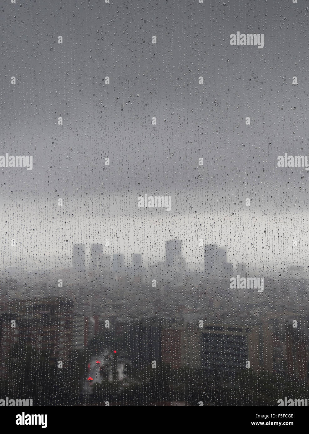 After heavy rainfall, the diffuse skyline of Barcelona is emerging in the twilight behind raindrops on a window. Stock Photo