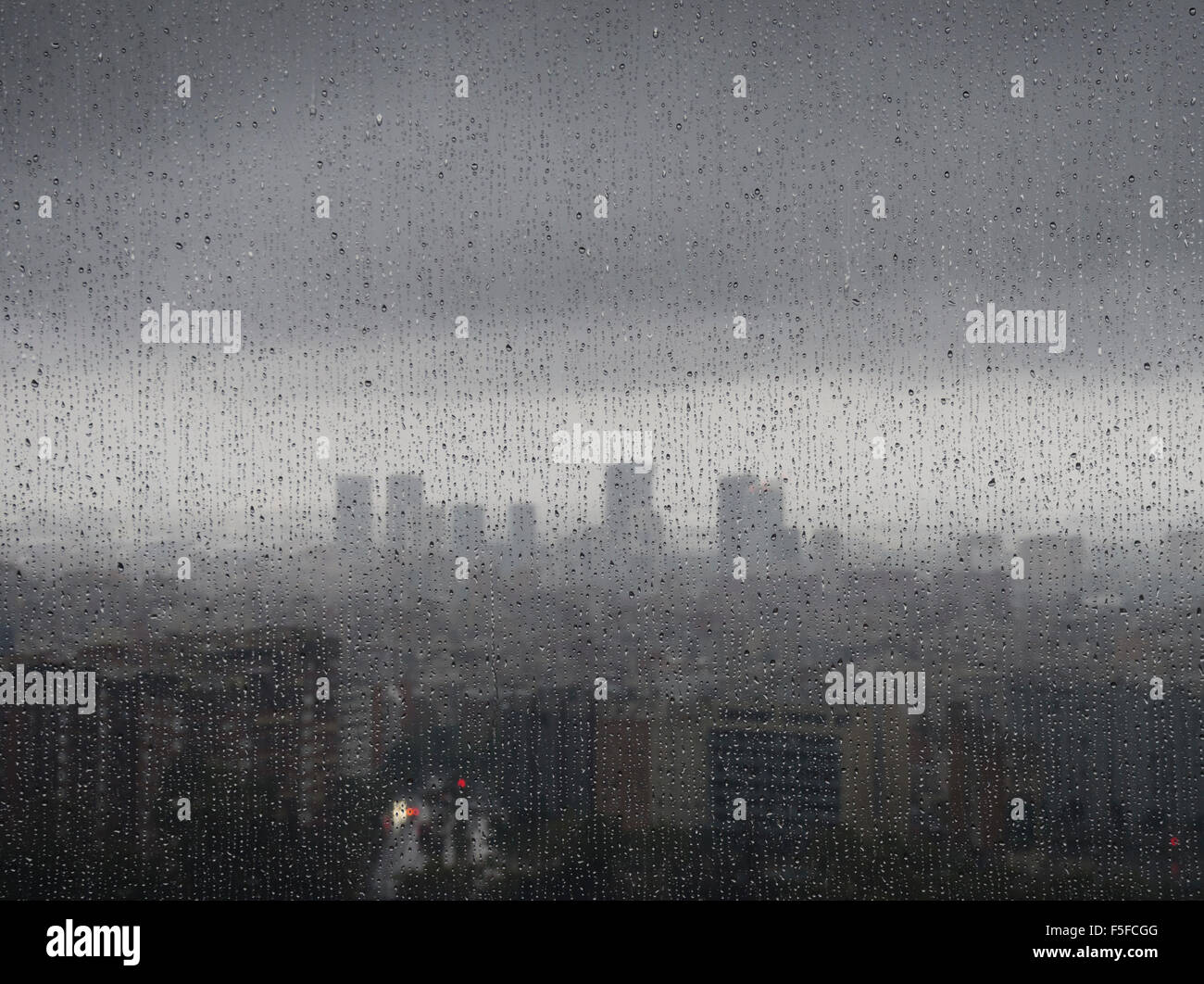 After heavy rainfall, the diffuse skyline of Barcelona is emerging in the twilight behind raindrops on a window. Stock Photo