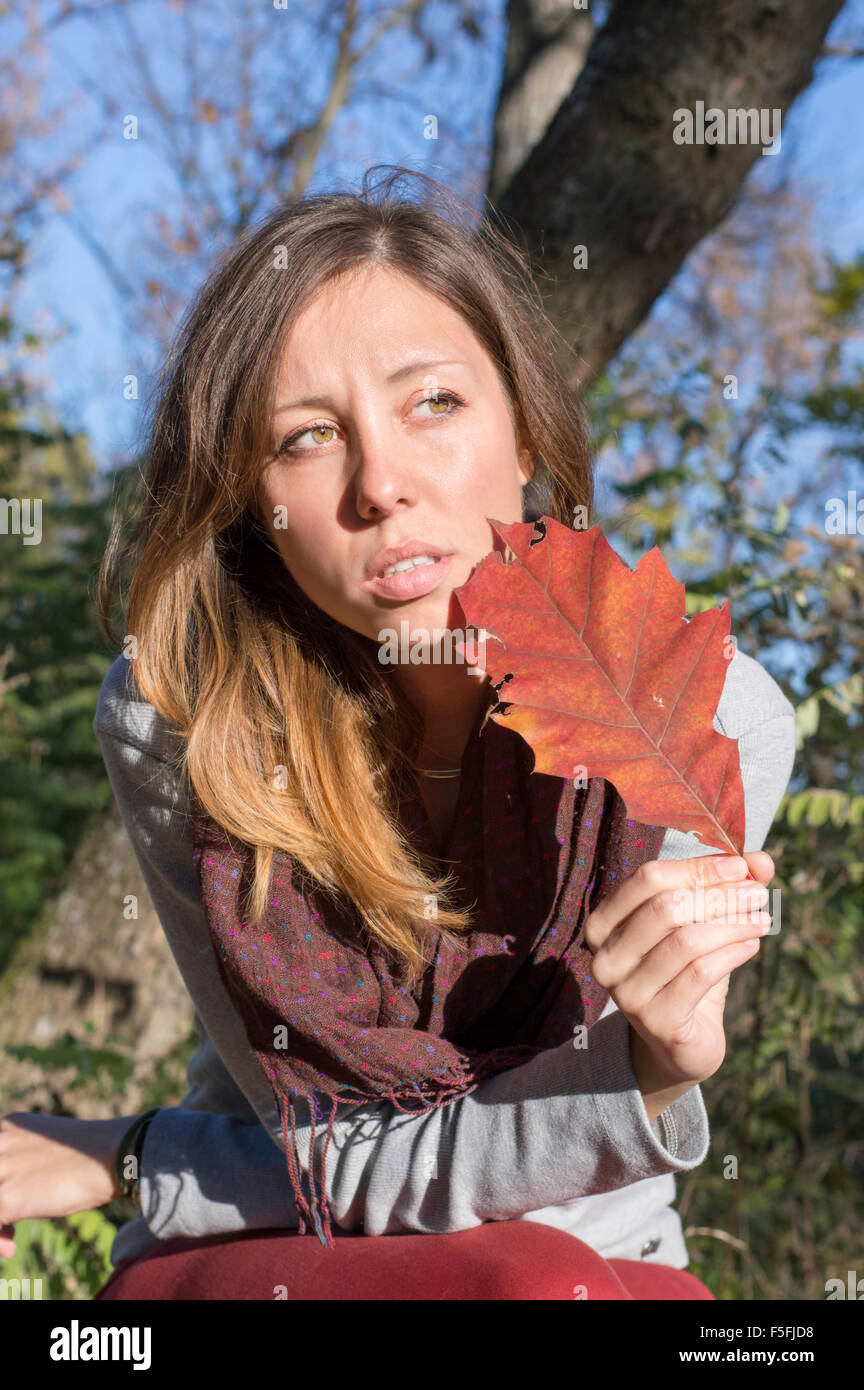 Sad girl holding red autumn leaf in her hand while sitting in the park Stock Photo
