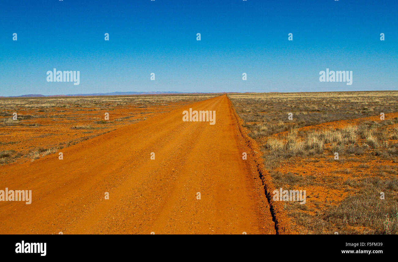 Long red dirt road in Australian outback stretching across arid treeless plains of  Flinders Ranges desert region to distant horizon & blue sky Stock Photo