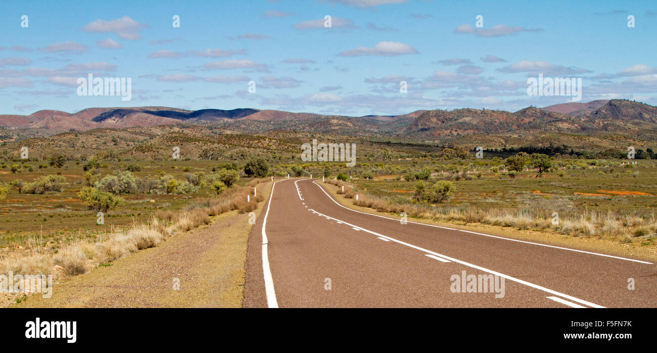 Panoramic view of highway slicing through vast outback landscape towards barren hills of Flinders Ranges rising into blue sky, South Australia Stock Photo