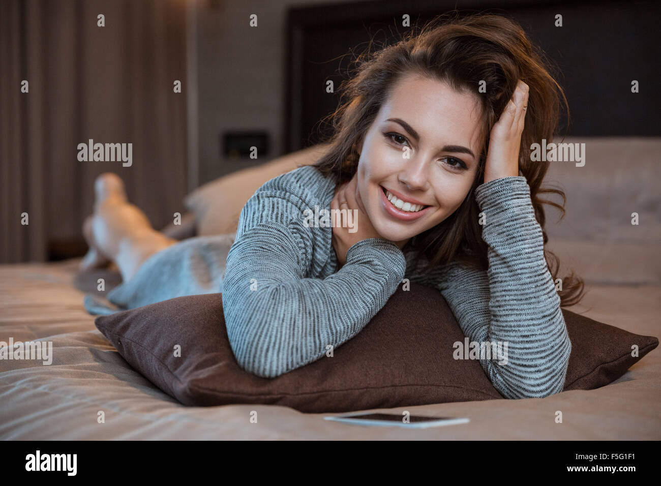 Portrait of a smiling pretty woman lying on the bed and looking at ...