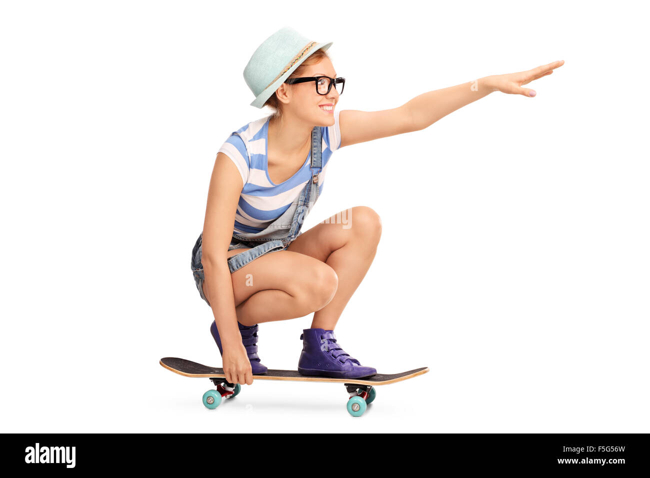 Profile shot of a hipster girl riding a skateboard and pointing forward with her hand isolated on white background Stock Photo
