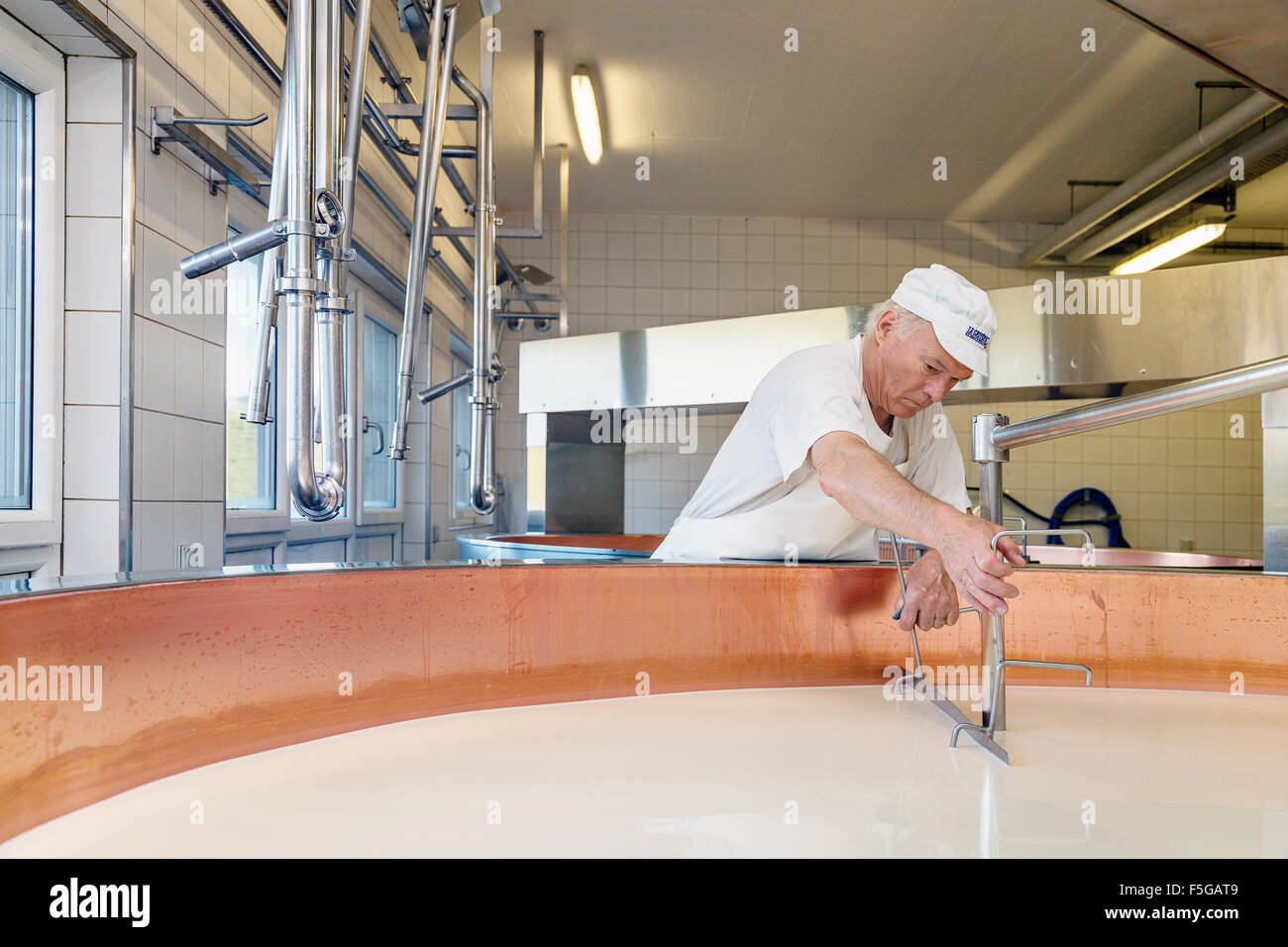 Cheese maker warming and mixing fresh milk into Le Gruyère cheese in dairy (cheese factory) in the village of Echarlens. Gruyère Stock Photo