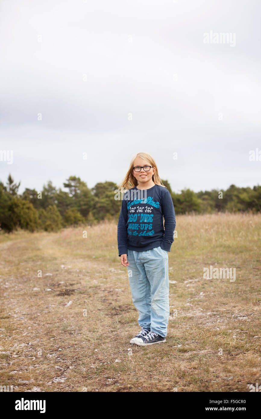 A pretty 9-year-old girl is standing in a field in a rural area on
