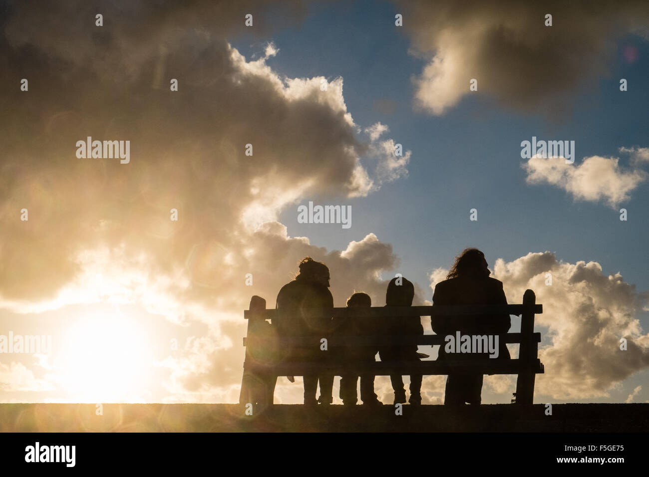 Family,as a silhouette eating fish and chips on a bench on a windy sunny day at Borth,Ceredigion,Wales,U.K.,clouds,weather, Stock Photo