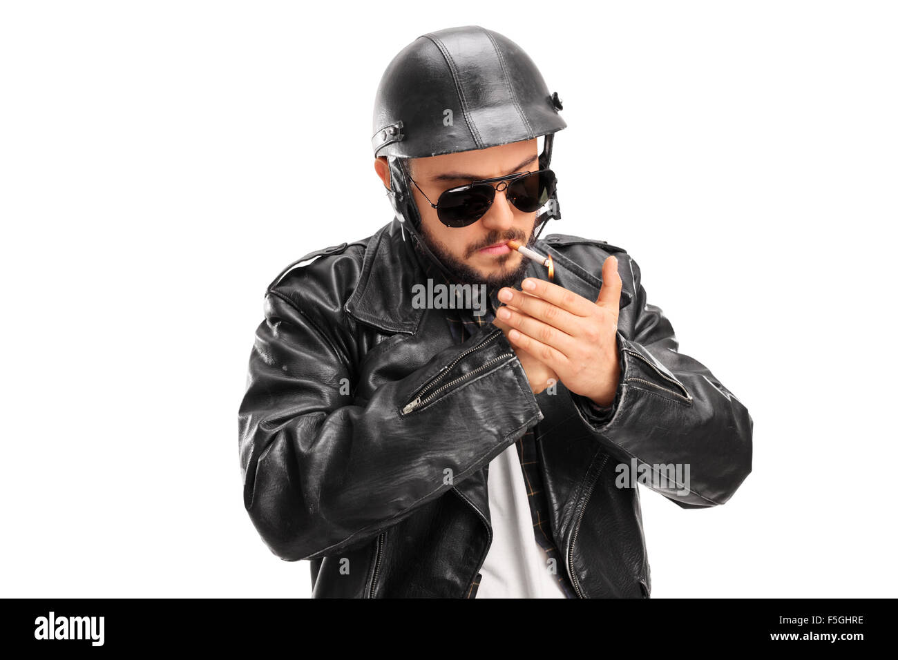 Studio shot of a male biker in a black leather jacket lighting up a cigarette with a lighter isolated on white background Stock Photo