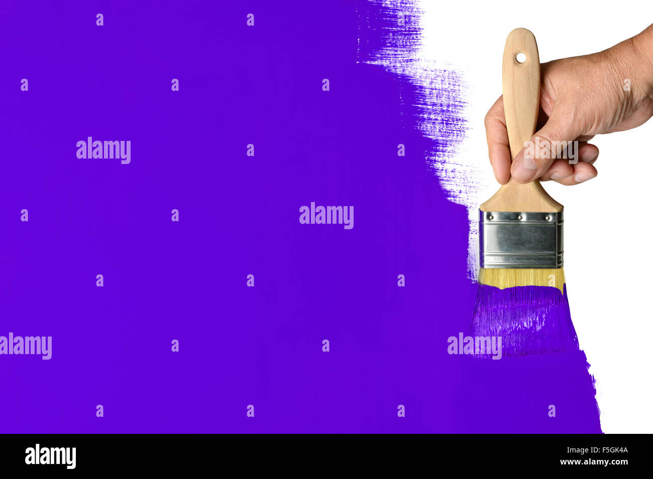 Man's hand using paintbrush with purple paint on wall Stock Photo