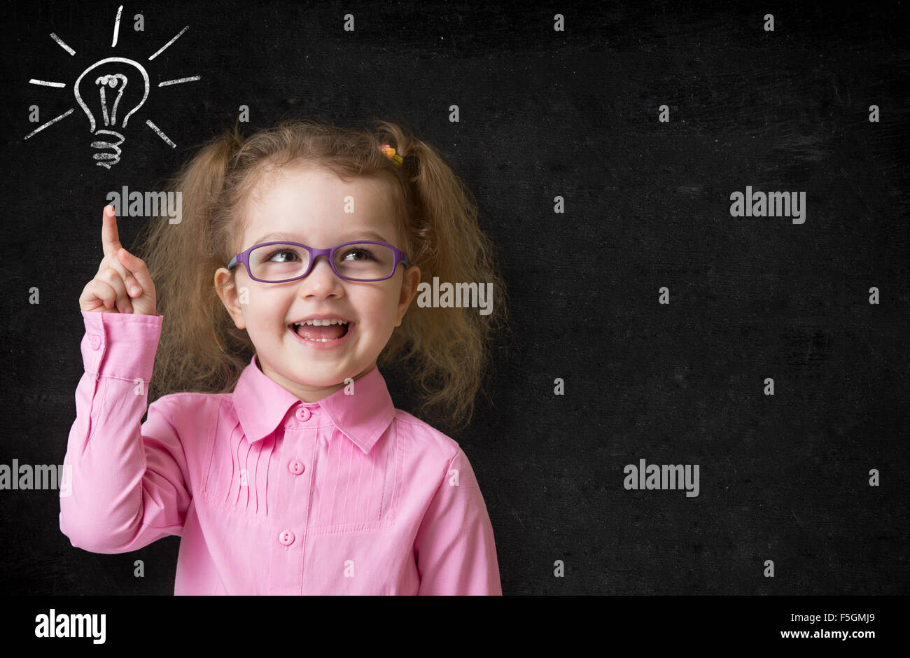 kid in glasses with idea lamp on school chalkboard Stock Photo