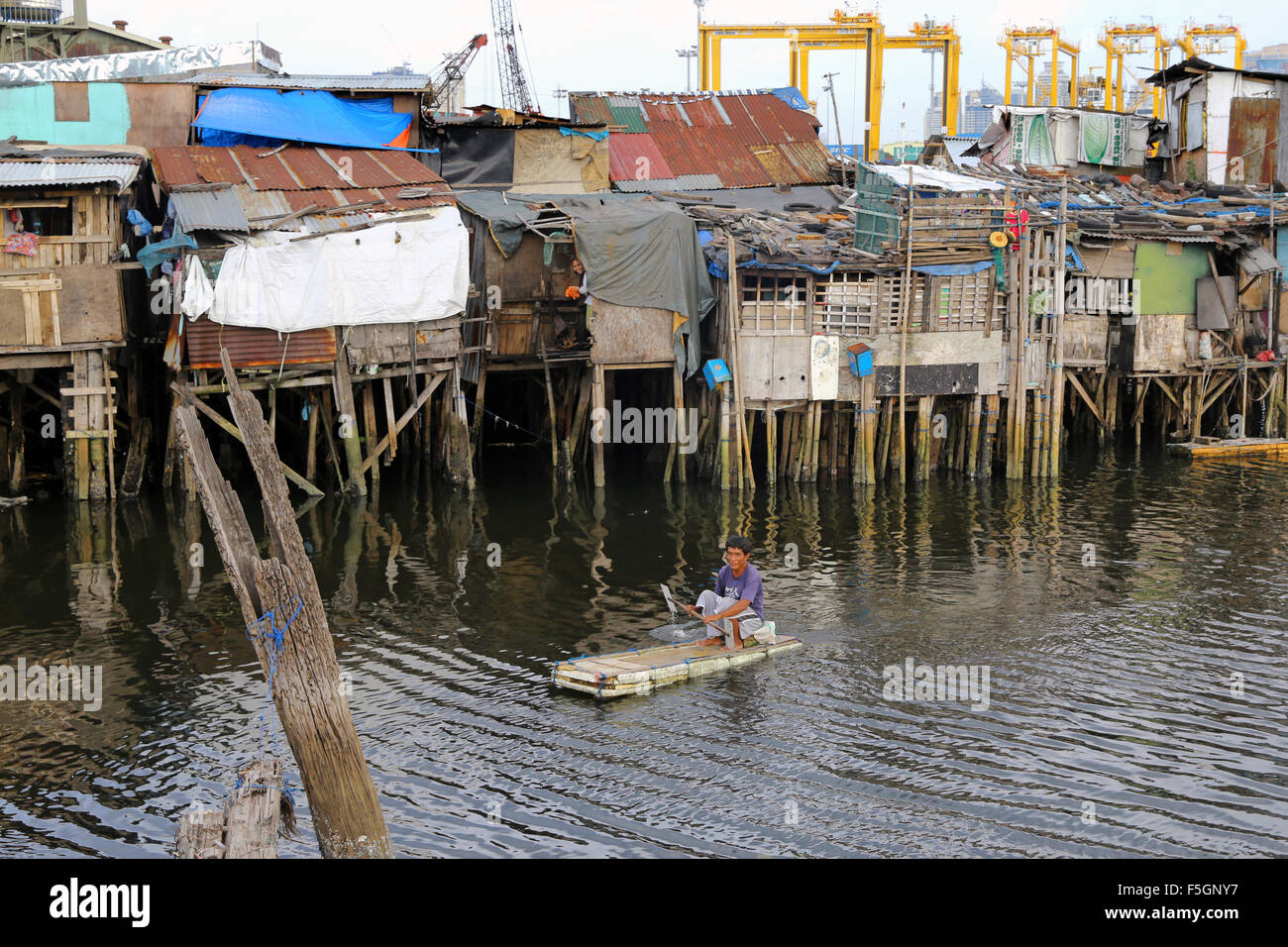 Manila, The Philippines: Resident of a poor neighborhood living in huts on stilts with firewood on a Styrofoam float, Tondo township, Manila, Philippines Stock Photo