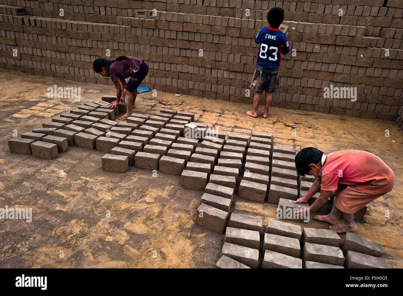 Peruvian children collect raw bricks for burning at a brick factory in Huachipa, a suburb in the outskirts of Lima, Peru. Stock Photo