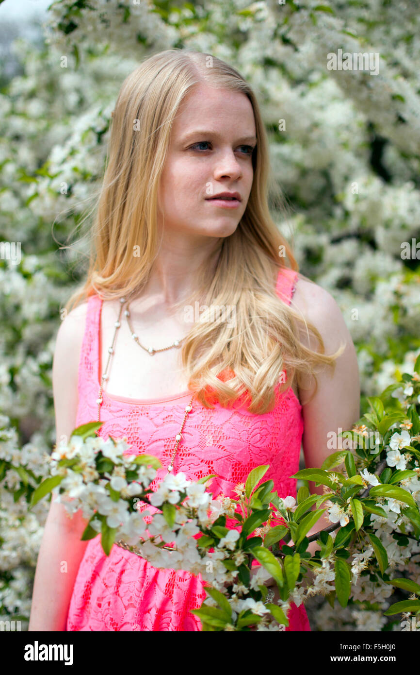 Blonde woman in a pink dress posing within flowers during the summer. Stock Photo