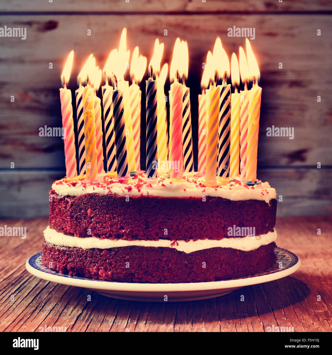 a cake topped with some lit candles before blowing out the cake, on a rustic wooden table, with a filtered effect Stock Photo