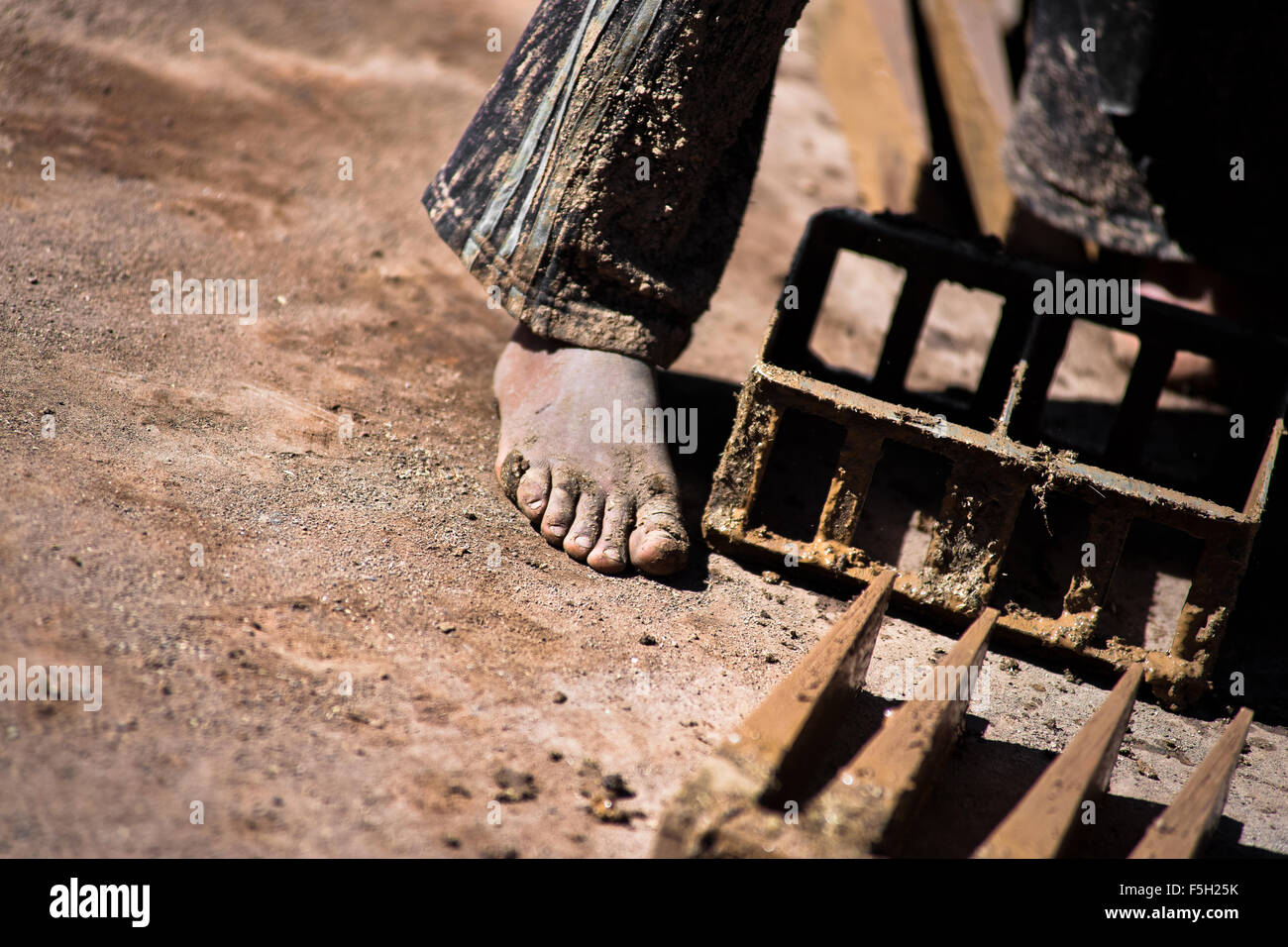 A Peruvian boy, working barefoot, molds bricks of clay at a brick factory in the outskirts of Puno, Peru. Stock Photo