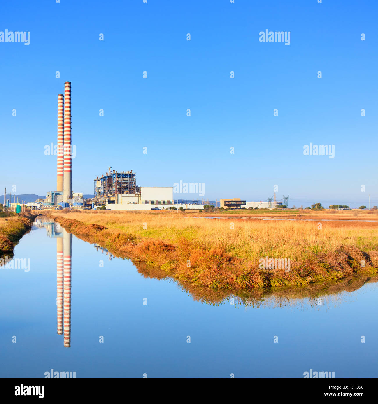 Power plant with two smoke stacks, green field and reflection on water Stock Photo