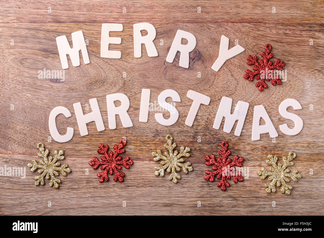 merry christmas made with wooden letters on wood with gold and red snowflake decorations Stock Photo