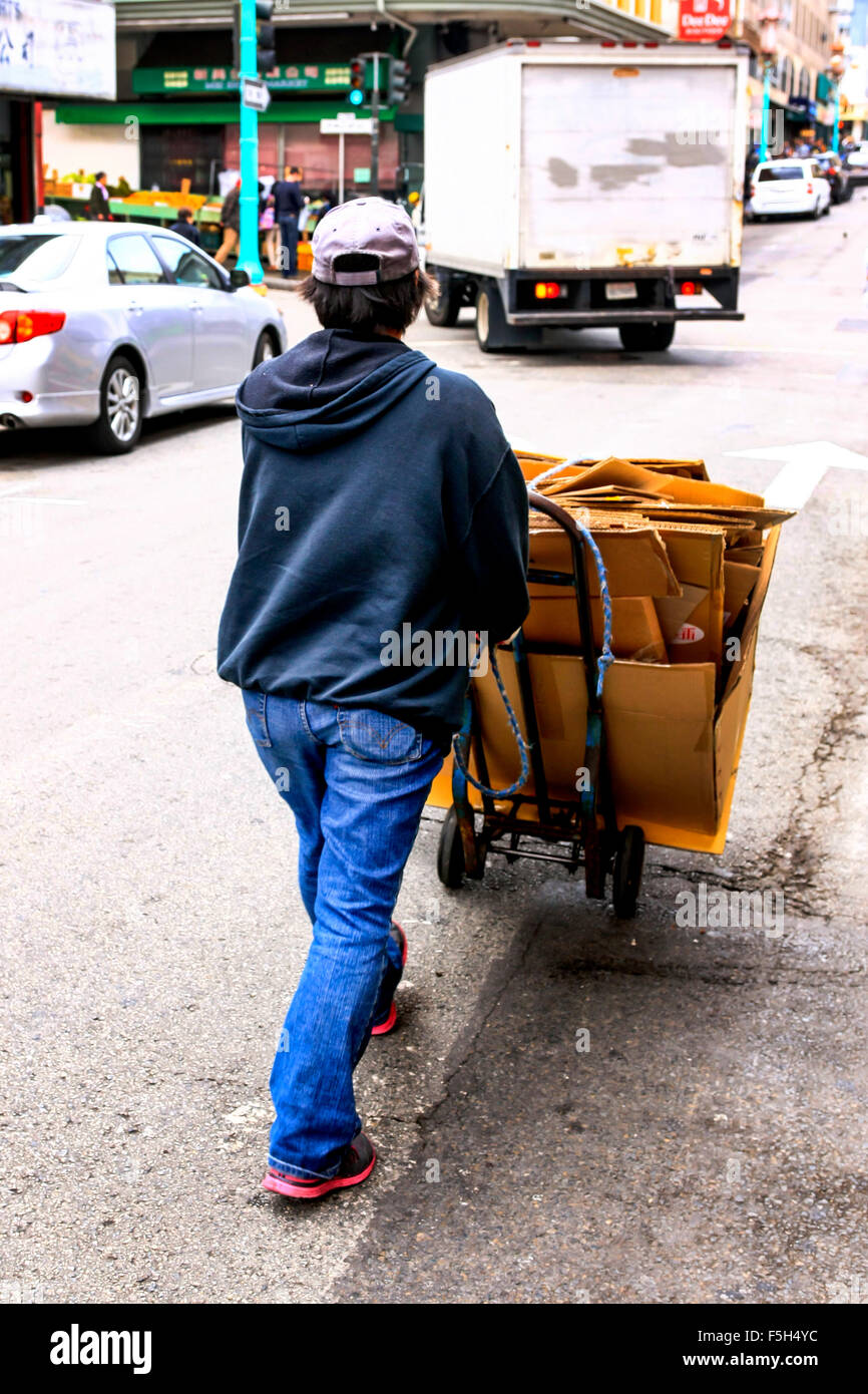 Chinese man pushing a sack-truck loaded with used cardboard boxes through the streets of Chinatown in San Francisco CA Stock Photo