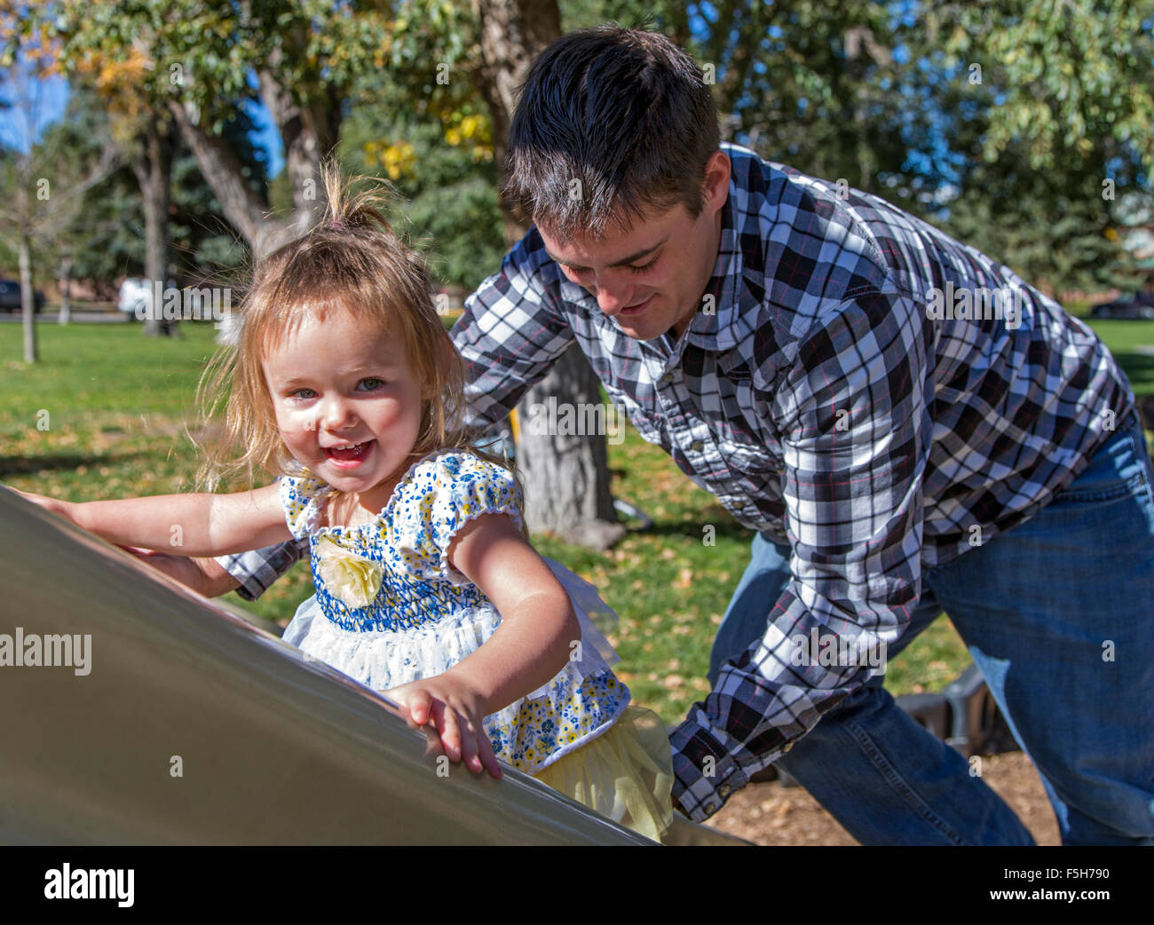Father and young daughter playing on a sliding board, park playground Stock Photo
