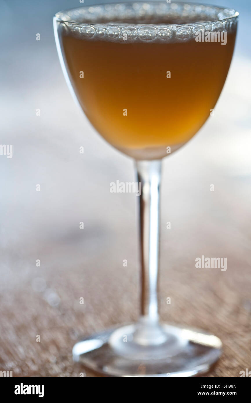 an amber cocktail in a stemmed glass on wood, backlit Stock Photo
