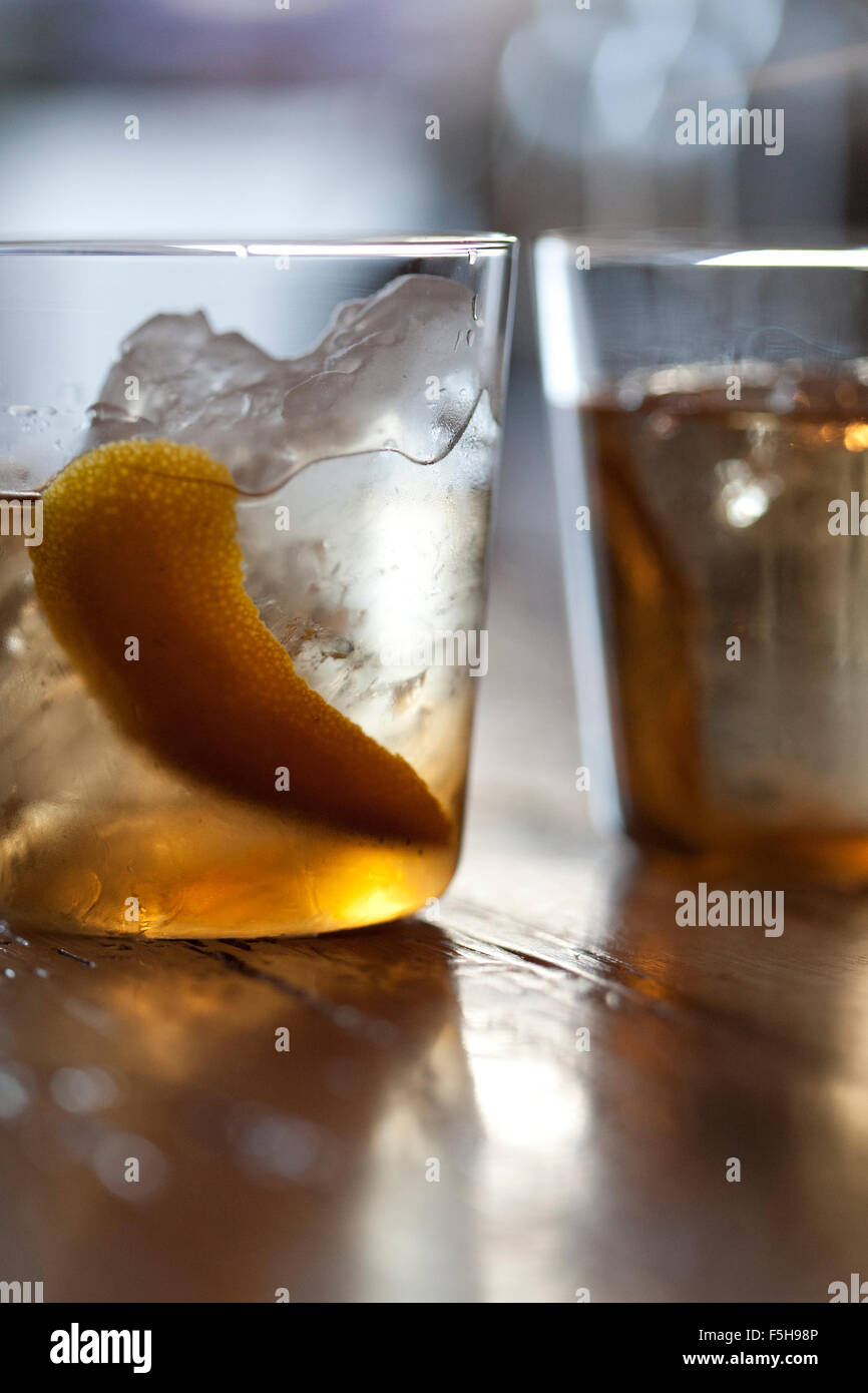 two cocktails,  one cropped, both with ice and lemon peel on a wood surface Stock Photo