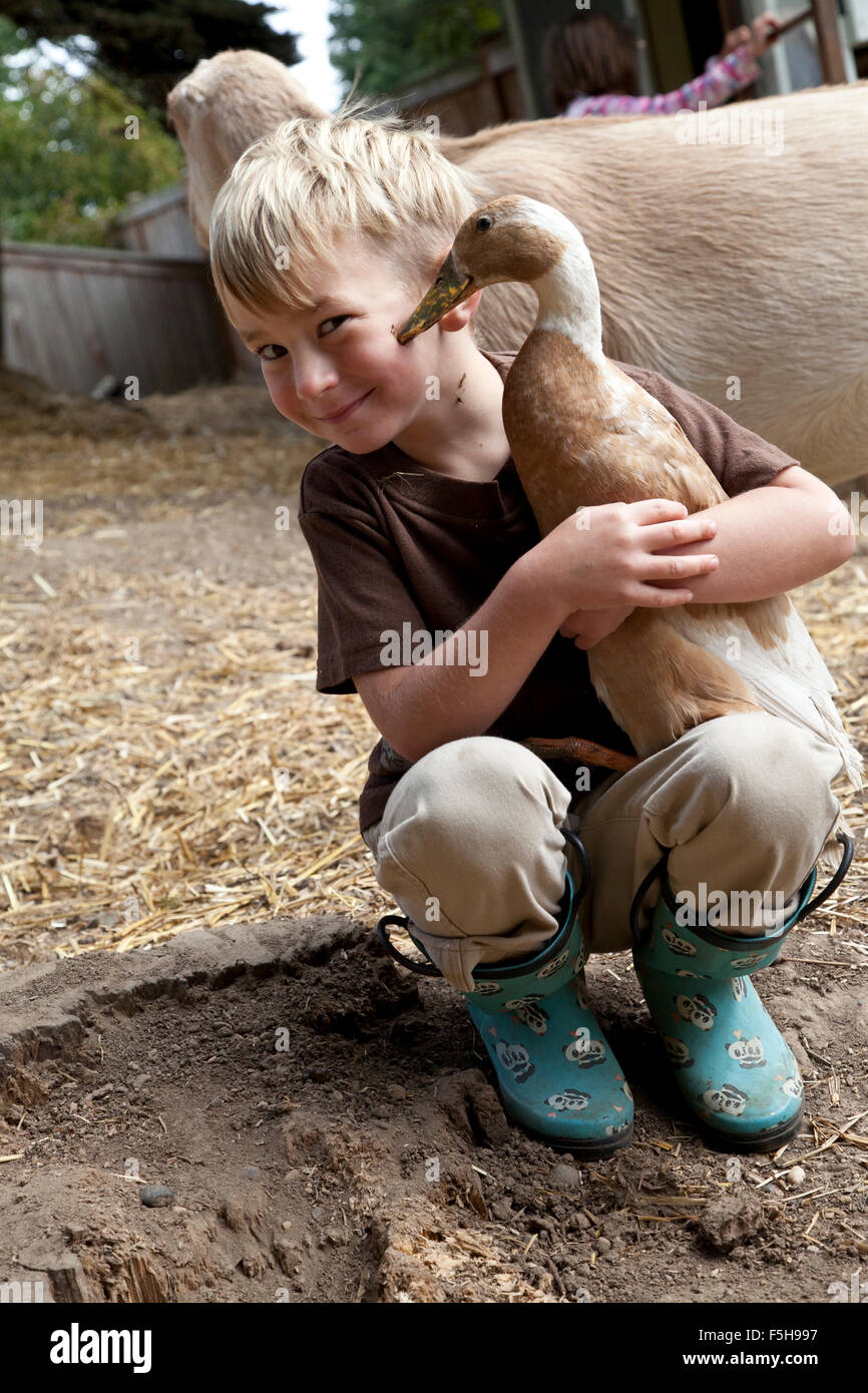 a small boy holding a duck smiles and looks at the camera as the duck touches its beak to the boy's cheek Stock Photo