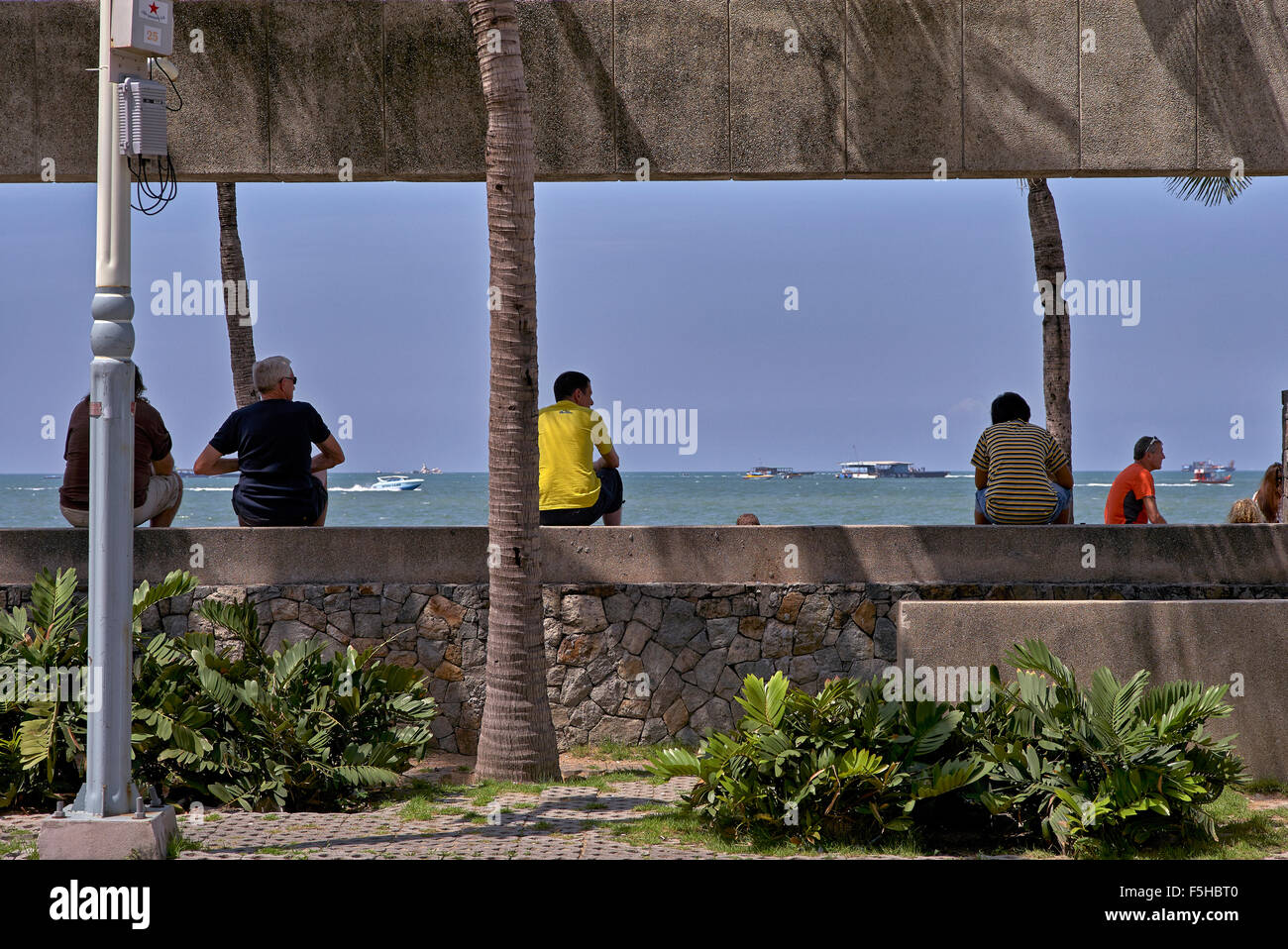 People passing the time of day sitting on a wall with an ocean overview. Pattaya Thailand S. E. Asia Stock Photo