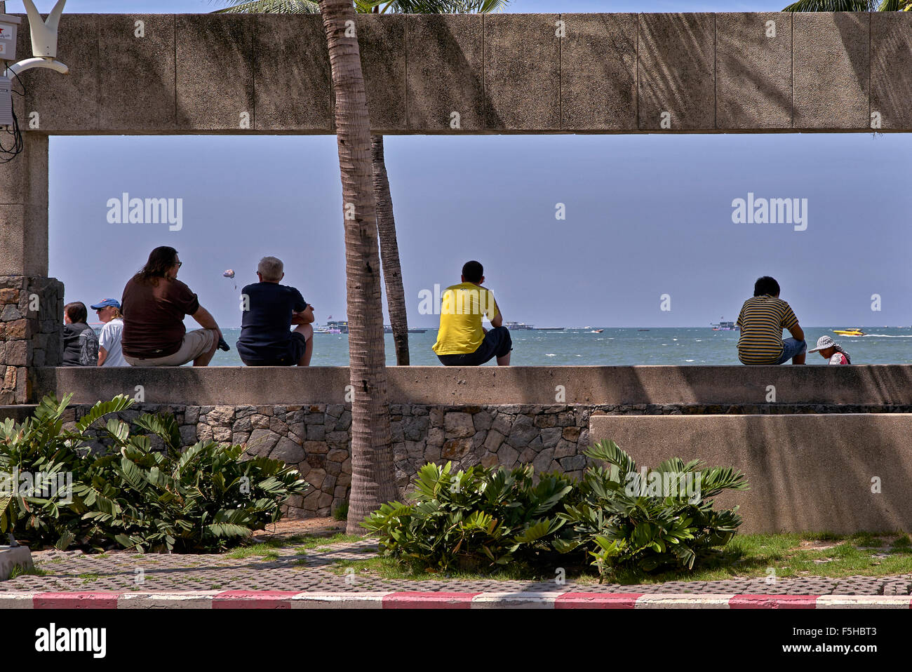 People passing the time of day sitting on a wall with an ocean overview. Pattaya Thailand S. E. Asia Stock Photo