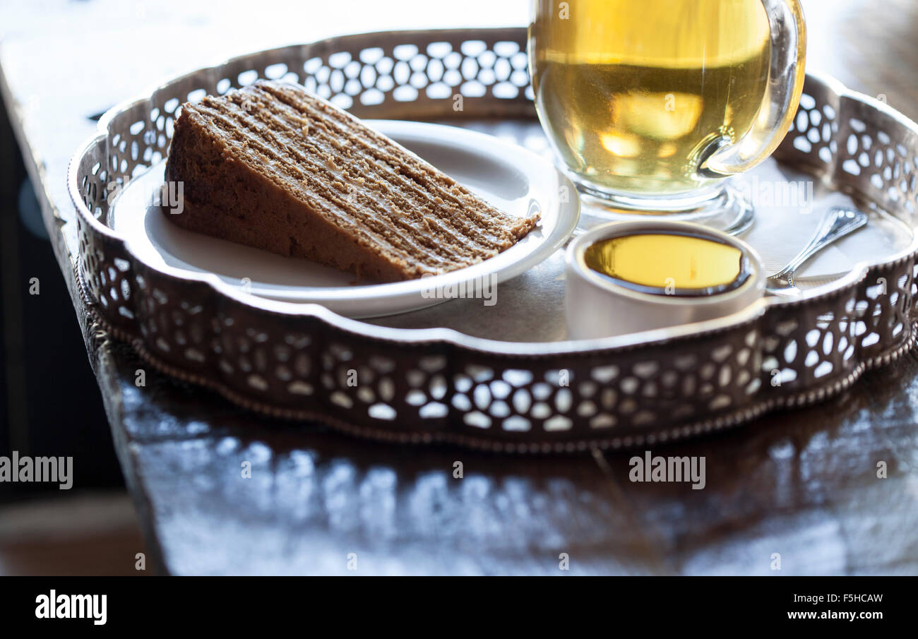Low angle shot of honey cake and tea on silver platter, backlit Stock Photo